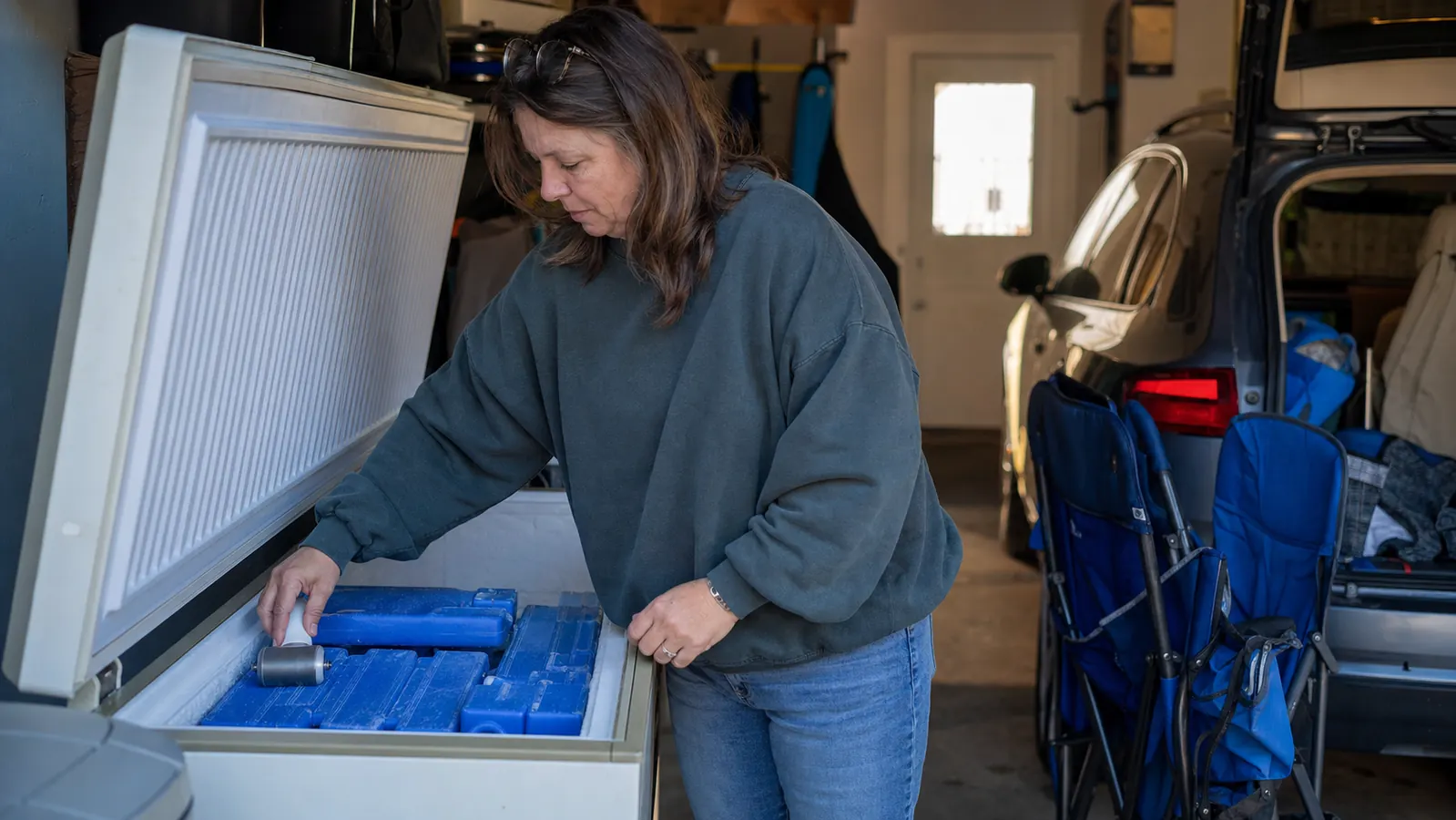 A garage chest freezer with a small ice roller sitting on top of stacked reusable ice packs
