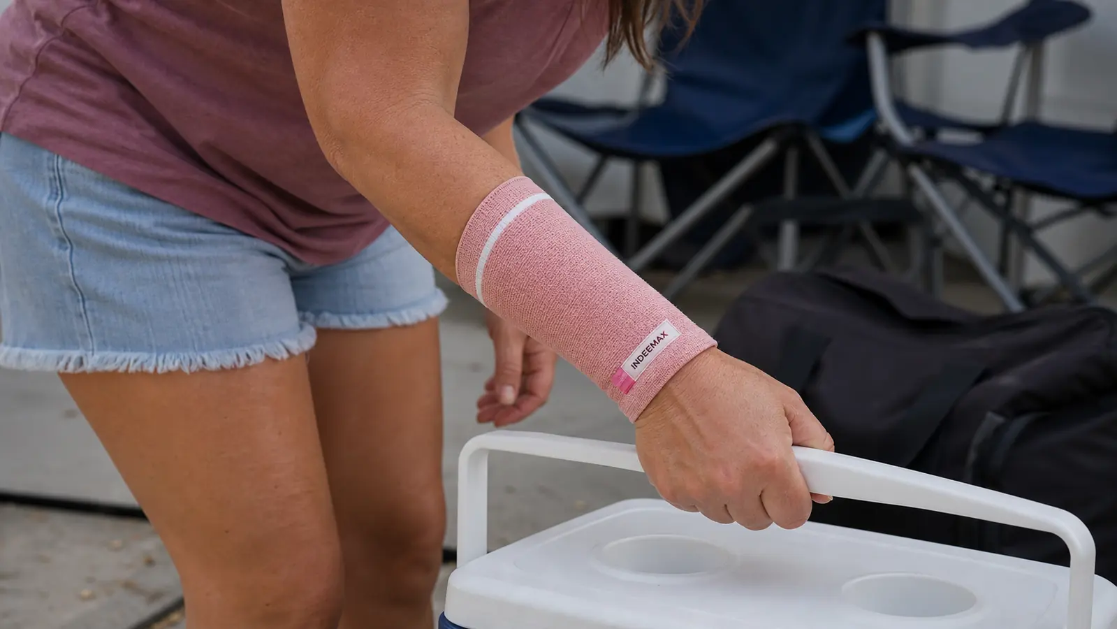 A close up of a hand wearing a black copper toned wrist compression sleeve gripping the handle of a cooler
