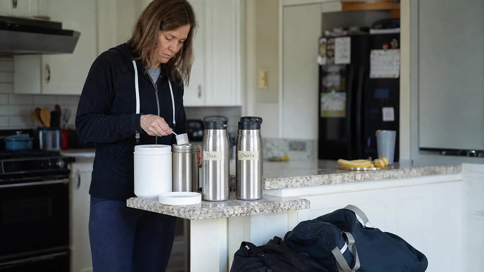 A tub of unflavored L-Glutamine powder on a kitchen counter next to two labeled water bottles, morning light through the window