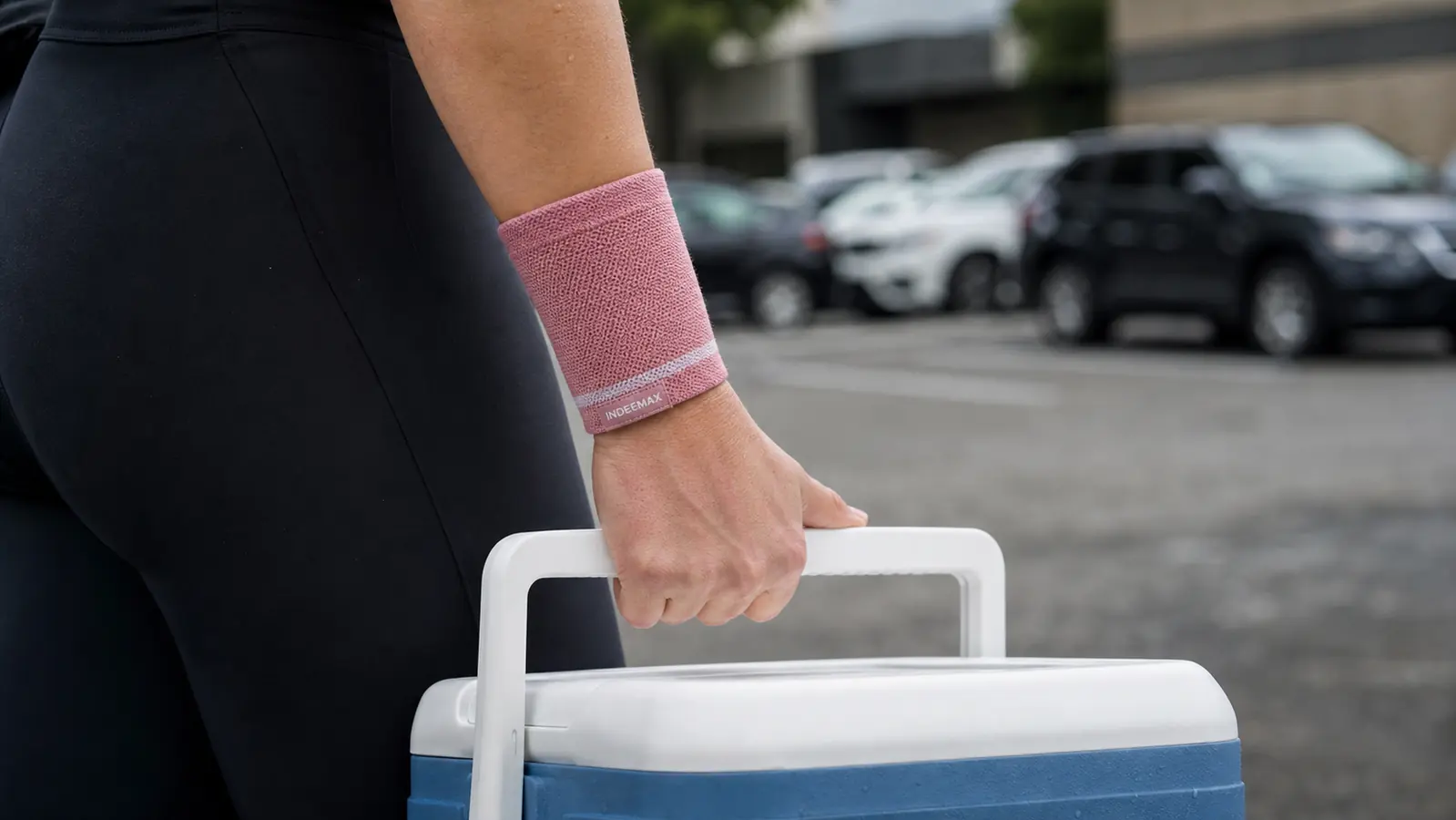 Hand wearing a copper toned wrist compression sleeve gripping the handle of a loaded ice chest